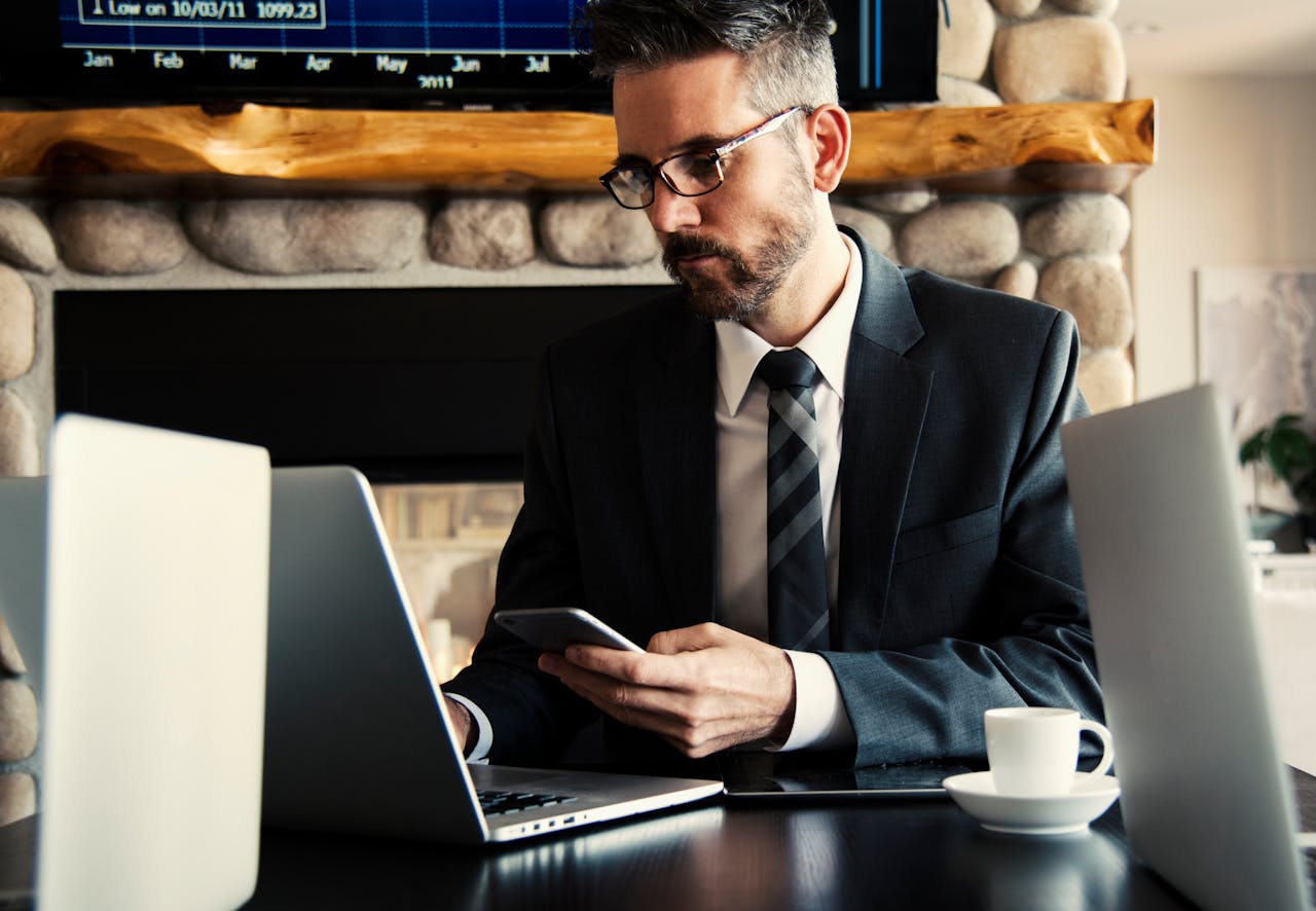 Home Businessman in formal attire working on a laptop and smartphone at an indoor office desk.